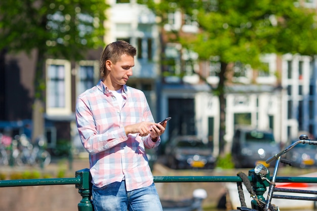 Jonge blanke man schrijven bericht per telefoon buiten in Europese stad