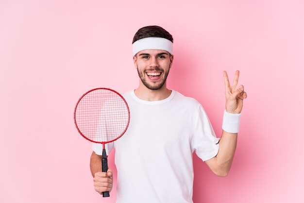 Jonge blanke man spelen badminton geïsoleerd vrolijk en zorgeloos met een vredessymbool met vingers.