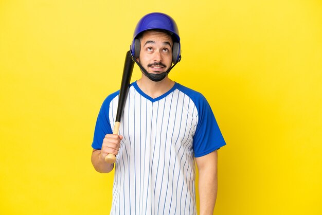 Jonge blanke man spelen honkbal geïsoleerd op gele achtergrond en opzoeken