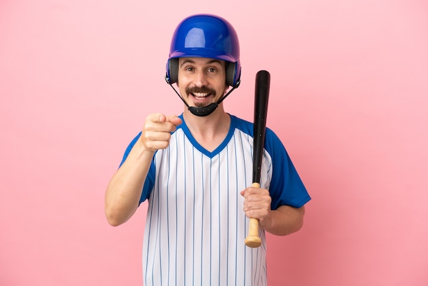 Jonge blanke man spelen honkbal geïsoleerd op roze achtergrond verrast en wijzend naar voren