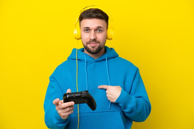 Jonge blanke man spelen met een video game controller geïsoleerd op gele achtergrond met verrassende gezichtsuitdrukking