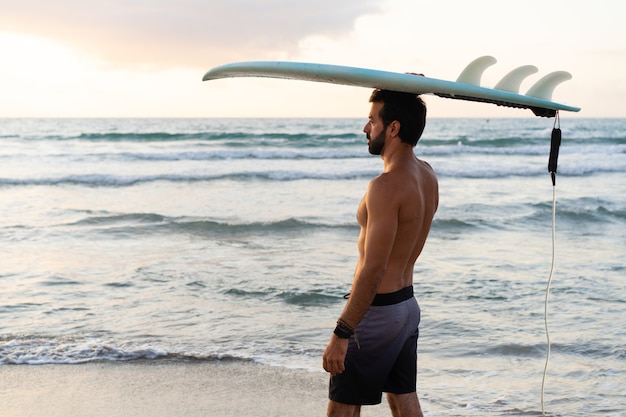 Jonge blanke man staat vroeg op om te surfen bij zonsopgang