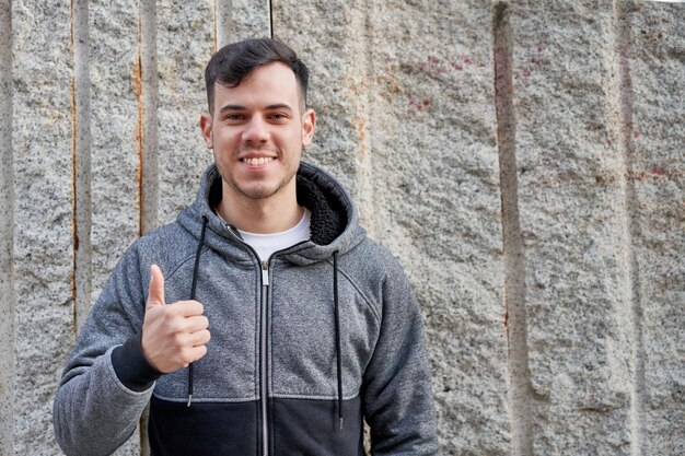 Jonge blanke man straalt koelte uit terwijl hij tegen een muur op straat leunt