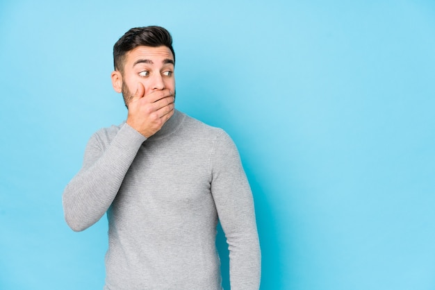 Jonge blanke man tegen een blauwe achtergrond geïsoleerd nadenkend op zoek naar een kopie ruimte die mond bedekt met hand.