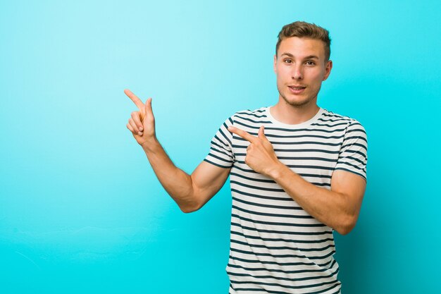 Jonge blanke man tegen een blauwe muur geschokt wijzend met wijsvingers naar een kopie ruimte.