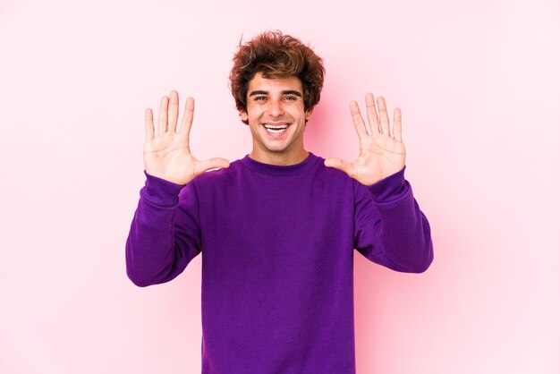 Jonge blanke man tegen een roze muur geïsoleerd met nummer tien met handen.