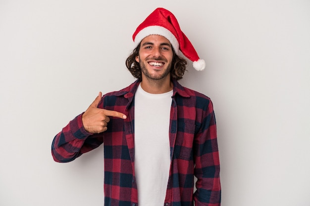 Jonge blanke man viert Kerstmis geïsoleerd op een grijze achtergrond persoon die met de hand wijst naar een shirt kopieerruimte, trots en zelfverzekerd