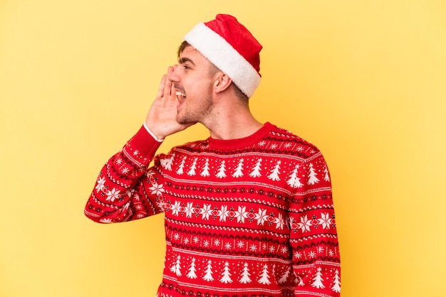 Jonge blanke man viert kerstmis geïsoleerd op gele achtergrond schreeuwen en houden palm in de buurt van geopende mond.