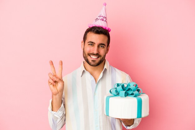 Jonge blanke man viert zijn verjaardag geïsoleerd op roze muur met nummer twee met vingers