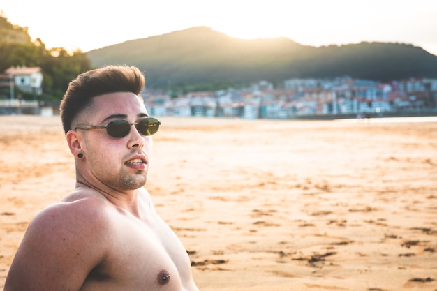 Jonge blanke man zit op het zand van een baskisch strand.