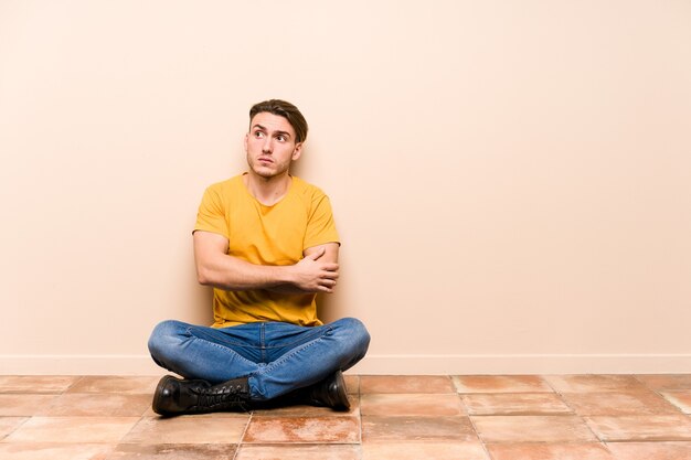 Jonge blanke man zittend op de vloer geïsoleerd ongelukkig vooraan kijken met sarcastische uitdrukking.
