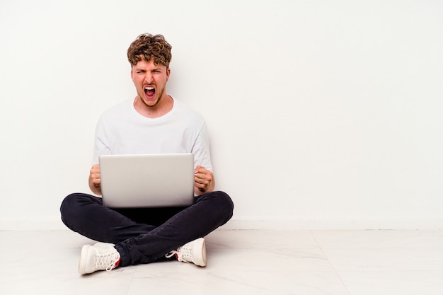 Jonge blanke man zittend op de vloer houden op laptop geïsoleerd op een witte achtergrond schreeuwen erg boos en agressief.