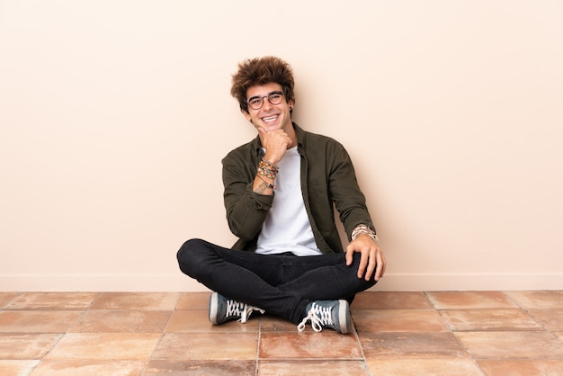Jonge blanke man zittend op de vloer met een bril en glimlachen