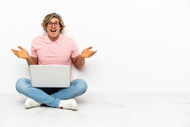 Foto jonge blanke man zittend op de vloer met zijn laptop geïsoleerd