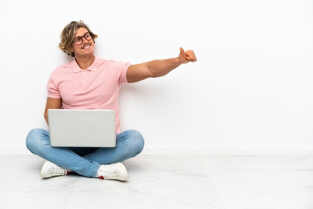 Jonge blanke man zittend op de vloer met zijn laptop geïsoleerd