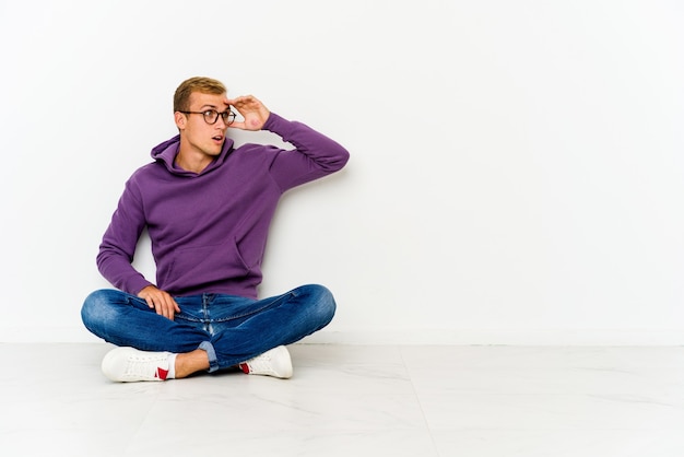 Jonge blanke man zittend op de vloer op zoek ver weg hand houdend op het voorhoofd.