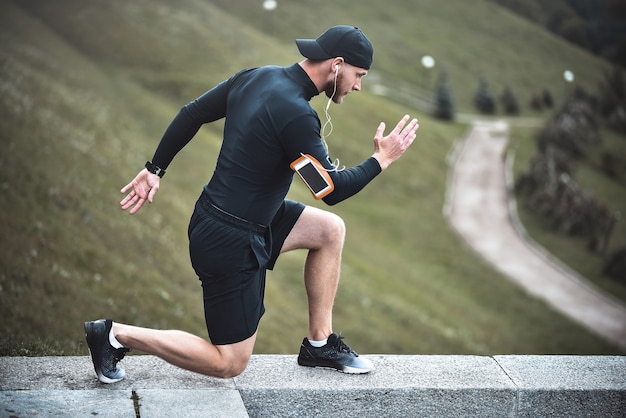 Jonge blanke mannelijke jogger met fitness-tracker bevestigd aan arm doet opwarmen voordat hij gaat joggen.