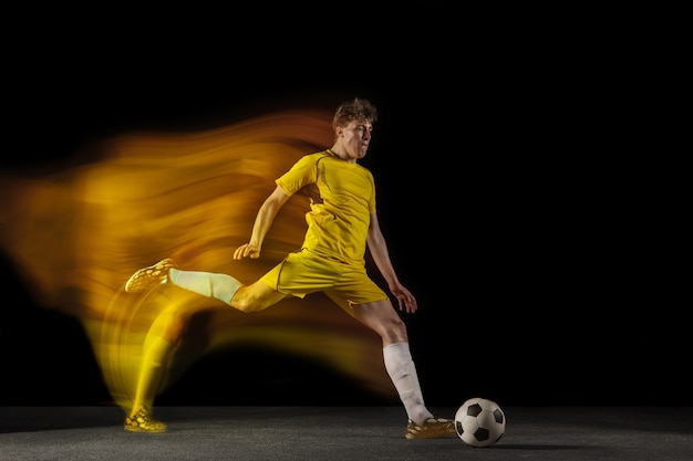 Jonge blanke mannelijke voetbal of voetballer schoppen bal voor het doel in gemengd licht op donkere muur concept van gezonde levensstijl professionele sport hobby