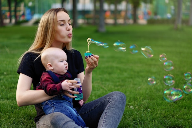 Jonge blanke moeder opgeblazen zeepbellen met haar zoontje in een park op een zonnige zomerdag.