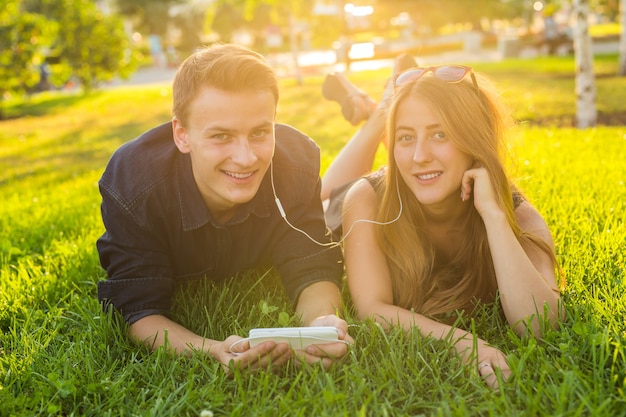 Jonge blanke mooie paar of studenten liggen samen op het gras, luisteren naar muziek. liefde, relatie, zomer en lifestyle concept.