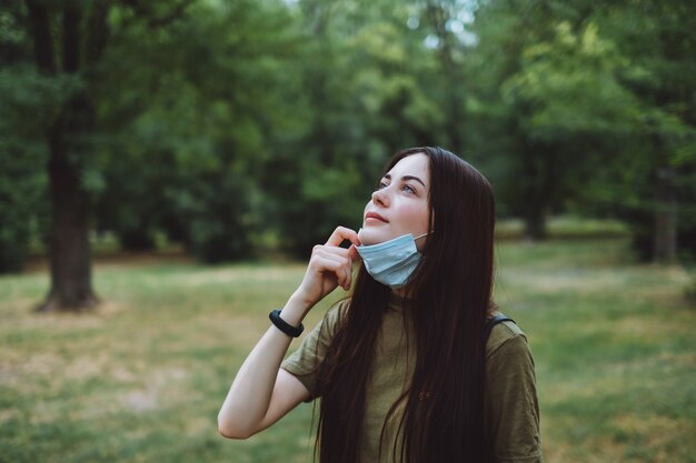 Jonge blanke mooie vrouw verwijdert een medisch beschermend masker op de natuur, schone frisse lucht inademen.