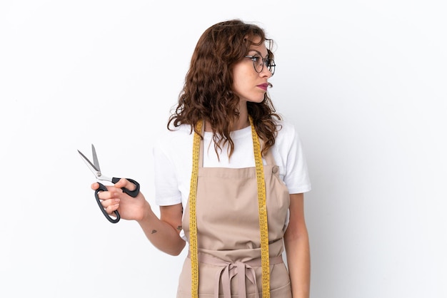 Foto jonge blanke naaister vrouw geïsoleerd op een witte achtergrond op zoek naar de kant