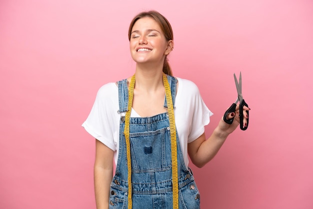 Jonge blanke naaister vrouw geïsoleerd op roze achtergrond lachen