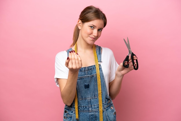 Jonge blanke naaistervrouw geïsoleerd op roze achtergrond die uitnodigt om met de hand te komen Blij dat je bent gekomen