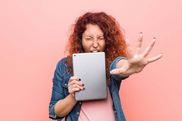 Jonge blanke roodharige vrouw met een tablet schreeuwen opgewonden aan de voorkant.