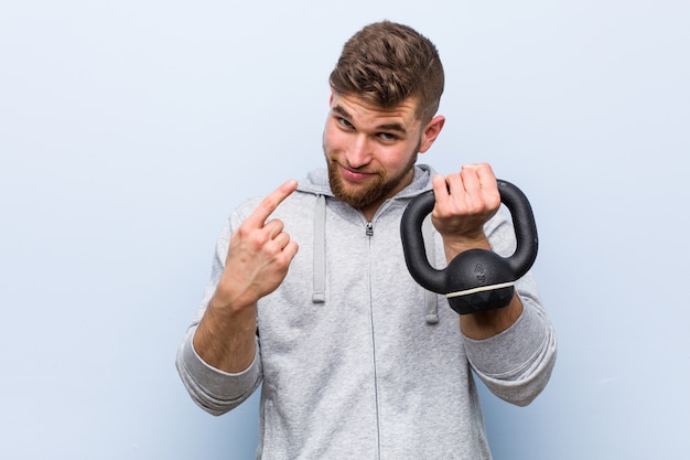 Jonge blanke sportman die een halter houdt die met de vinger naar je wijst alsof ze dichterbij komen.