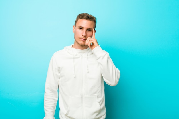 Jonge blanke sportman wijzende tempel met vinger, denken, gericht op een taak.