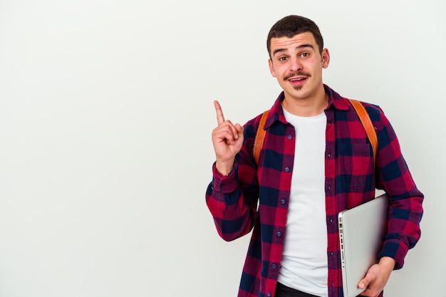 Jonge blanke student man met een laptop geïsoleerd op wit glimlachend vrolijk wijzend met wijsvinger weg.