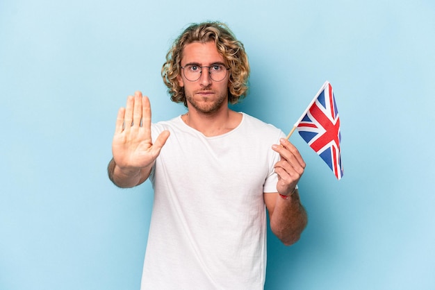 Jonge blanke student man met een vlag van het Verenigd Koninkrijk geïsoleerd op een blauwe achtergrond staande met uitgestrekte hand weergegeven: stopbord, voorkomen dat je.