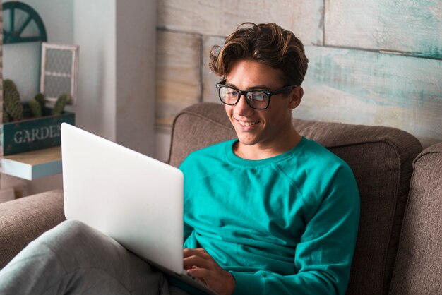 Jonge blanke student studeert thuis met internet en laptopcomputer zittend op de bank