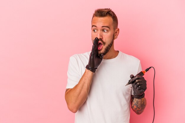 Jonge blanke tatoeëerder geïsoleerd op roze achtergrond zegt een geheim heet remnieuws en kijkt opzij