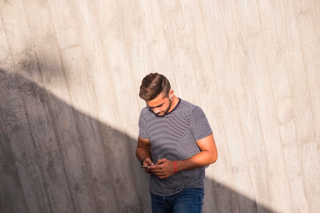 Jonge blanke tiener man gebruikt de telefoon om contact te maken met vrienden en e-mails en sociale media te controleren op internet licht en schaduw compositie op de stedelijke stadsmuur achtergrond