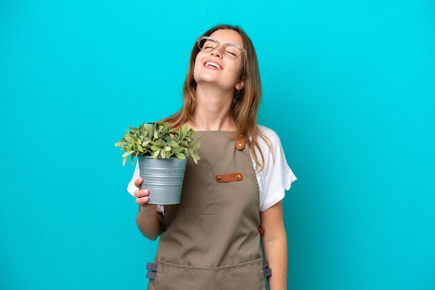 Jonge blanke tuinman vrouw met een plant geïsoleerd op blauwe achtergrond lachen