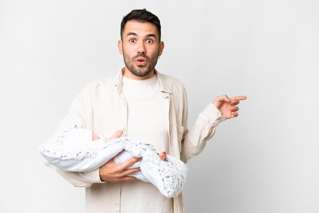 Jonge blanke vader met haar pasgeboren baby over geïsoleerde achtergrond verrast en wijzende kant