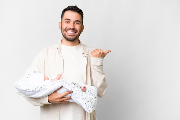 Jonge blanke vader met haar pasgeboren baby over geïsoleerde achtergrond wijzend naar de zijkant om een product te presenteren
