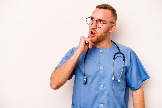 Foto jonge blanke verpleegster man geïsoleerd op een witte achtergrond zijwaarts kijkend met twijfelachtige en sceptische uitdrukking