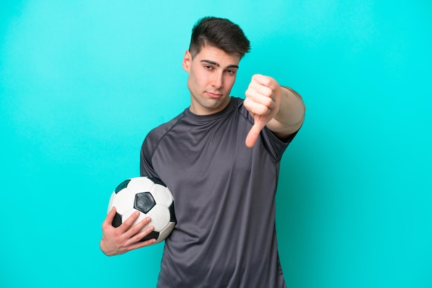 Jonge blanke voetballer man geïsoleerd op blauwe achtergrond met duim omlaag met negatieve expressie