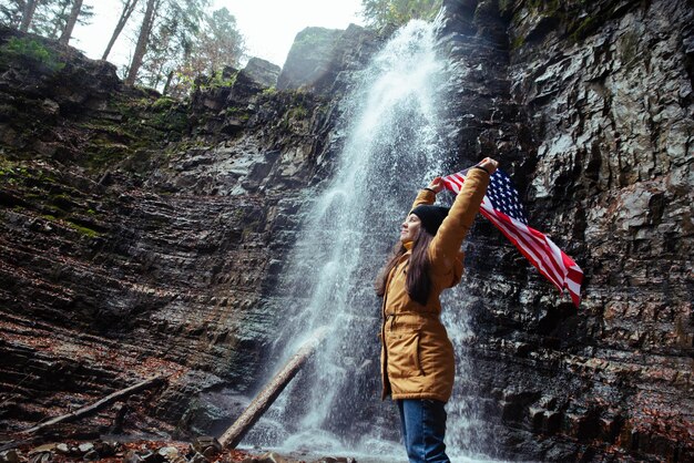 Jonge blanke volwassen vrouw met usa vlag voor waterval