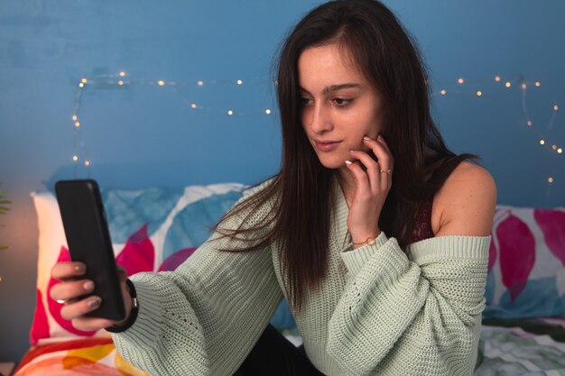 Jonge blanke vrouw aan het bed met behulp van de mobiele telefoon