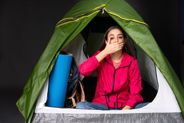 Jonge blanke vrouw binnen een camping groene tent die mond behandelt met handen