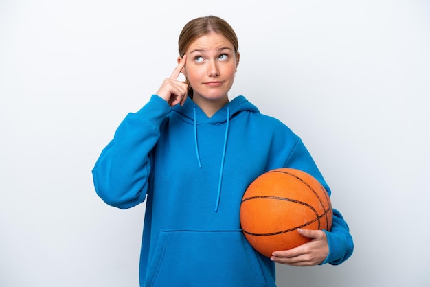 Jonge blanke vrouw die basketbal speelt geïsoleerd op een witte achtergrond die twijfels heeft en denkt