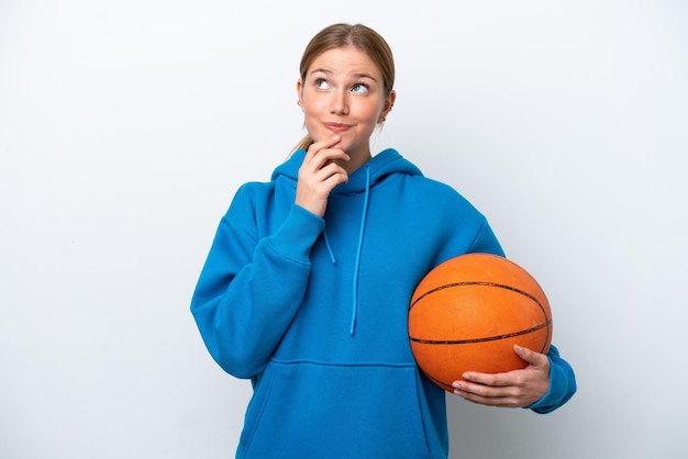 Jonge blanke vrouw die basketbal speelt geïsoleerd op een witte achtergrond terwijl ze glimlacht