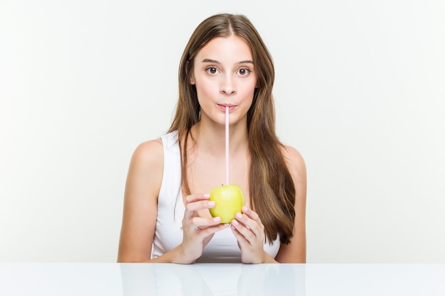 Jonge blanke vrouw die een appel met een rietje drinkt. Gezond leven concept.