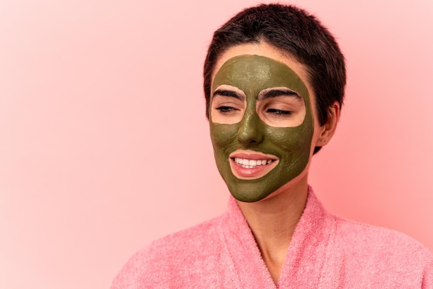 Jonge blanke vrouw die een gezichtsmasker draagt dat op roze achtergrond wordt geïsoleerd