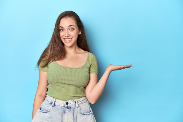 Jonge blanke vrouw die een kopieerruimte op een handpalm laat zien en een andere hand op de taille houdt