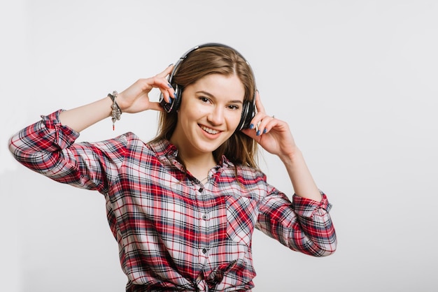 Jonge blanke vrouw die een koptelefoon draagt en muziek luistert op een grijze achtergrond